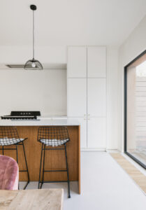 oude veranda wordt volwaardig volume naast half-open bebouwing- Architectuurbureau Friday Office For Architecture. Interieurbeeld van het houten kookeiland in de witte keuken naast een groot raam