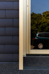 HOUSE SKIN door Friday office for architecture: facelift van rijwoning met nieuwe dakconstructie door monoliete gevel- en dakafwerking in donkerkleurige leien en goudkleurige raamkaders.