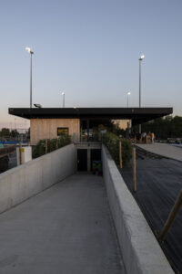 Nieuwbouw hockeyclub voor Royal victory Hockey in Edegem door Friday Office for architecture. Het nieuwe clublokaal, gefotografeerd bij valavond. Vooraan is een betonnen helingsbaan te zien die onder het clublokaal verdwijnt.