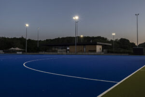 Nieuwbouw hockeyclub voor Royal victory Hockey in Edegem door Friday Office for architecture. Hockeyveld in schemering met op de achtergrond het nieuwe clublokaal.
