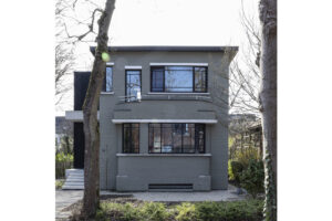 Deze vrijstaande woning in interbellumstijl krijgt een beglaasde uitbouw. Geïnspireerd op de horizontale detaillering in de voorbouw, is de nieuwe annex opgevat als plateaus die het gebouw omarmen. Ze dragen de leefruimte, keuken en badkamer, afgewerkt in glas en zwart gebeitst hout. Het ruime uitkragende overdekt terras geeft beschutting voor een heerlijk English breakfast in het groen.
