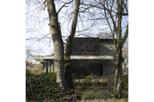 Deze vrijstaande woning in interbellumstijl krijgt een beglaasde uitbouw. Geïnspireerd op de horizontale detaillering in de voorbouw, is de nieuwe annex opgevat als plateaus die het gebouw omarmen. Ze dragen de leefruimte, keuken en badkamer, afgewerkt in glas en zwart gebeitst hout. Het ruime uitkragende overdekt terras geeft beschutting voor een heerlijk English breakfast in het groen.