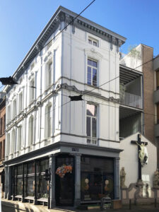 Verbouwing neoclassicistisch herenhuis door Friday Office for Architecture:Verbouwing van een neoclassicistisch herenhuis. hoekgebouw met klassieke witte gevel en sierlijsten, grote ramen en een winkel op de begane grond, gelegen aan een stadsstraat met bovenleidingen en aangrenzende moderne gebouwen.”
