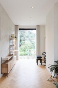 Renovatie van een gezinswoning door friday office for architecture. Een foto van de witte, lichte leefruimte met een groot raam dat uitzicht biedt op een groene omgeving.