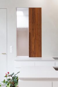 Renovatie van een gezinswoning door friday office for architecture. Detailfoto van het kruidenkastje in de keuken. Het kruidenkastje werd ingebouwd naast een raam dat uitgeeft op de inkomhal. Wanneer de deur van het kastje opengeschoven wordt, wordt het raam afgedekt door het deurtje.