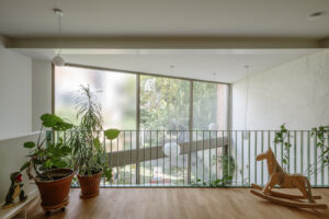 Lichte en open bovenverdieping met houten vloer, kamerplanten en grote ramen die uitkijken op de tuin. Deze moderne woninguitbreiding combineert natuurlijke materialen en zachte daglichtinval voor een rustgevende, eigentijdse leefruimte.