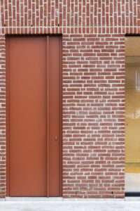 Bakstenen uitbouw aan een gezinswoning met grote schuifdeur en rode achterdeur door friday office for architecture.