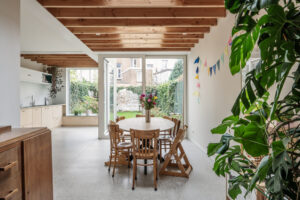 Renovatie van een gezinswoning door friday office for architecture. Achtergevel met licht-goude aluminiumbekleding. De lichte eetkamer geeft uit op de tuin en wordt gekenmerkt door een houten plafondstructuur die warmte uitstraalt en hier en daar geperforeerd is om zo buitenlicht binnen te laten.