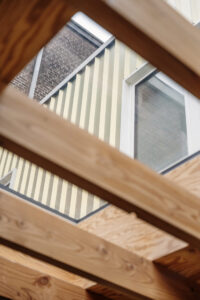 Renovatie van een gezinswoning door friday office for architecture. Achtergevel met licht-goude aluminiumbekleding. De lichte eetkamer geeft uit op de tuin en wordt gekenmerkt door een houten plafondstructuur die warmte uitstraalt en hier en daar geperforeerd is om zo buitenlicht binnen te laten.
