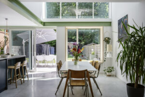renovatie van een gezinswoning door Friday office for architecture in Mortsel. Dubbelhoge leefruimte met ruime ramen die uitzicht bieden op de tuin. De bovenverdieping wordt gedragen. door karakteristieke groene liggers.