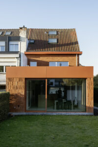 Renovatie van gezinswoning House Lion met geknikte zijgevel door Friday Office architecten. Dit is een beeld van de achtergevel. Op de foto staat de uitbouw van de woning in rode, speelse baksteen en rode kroonljst.