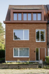 Renovatie van gezinswoning House Lion met geknikte zijgevel door Friday Office architecten. Foto van de voorgevel in rode baksteen met witte raamkaders en een rood, zinken dak met dakkapel.