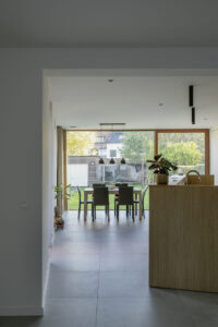 Renovatie van gezinswoning House Lion met geknikte zijgevel door Friday Office architecten. Interieurfoto van House Lion. zicht vanuit de leefruimte op de eetruimte en keuken met op de achtergrond een groot raam met zicht op de tuin.